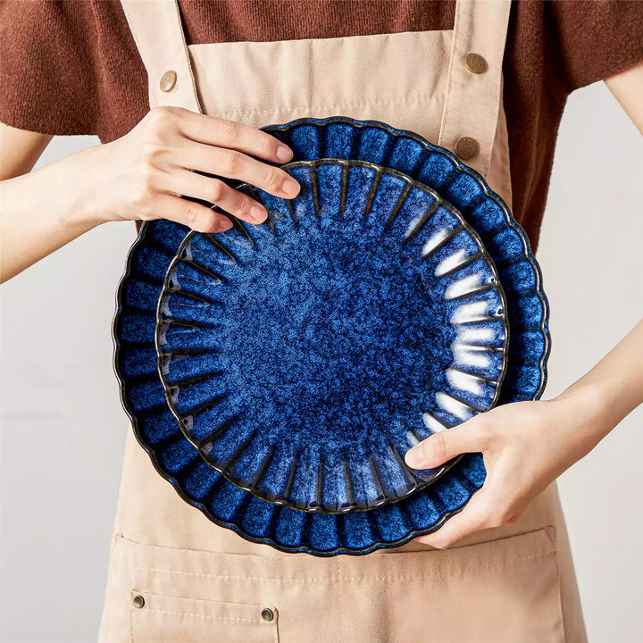 Adonis blue stoneware 16 piece dinnerware set model holding dinner plate and salad plate with chrysanthemum relief.