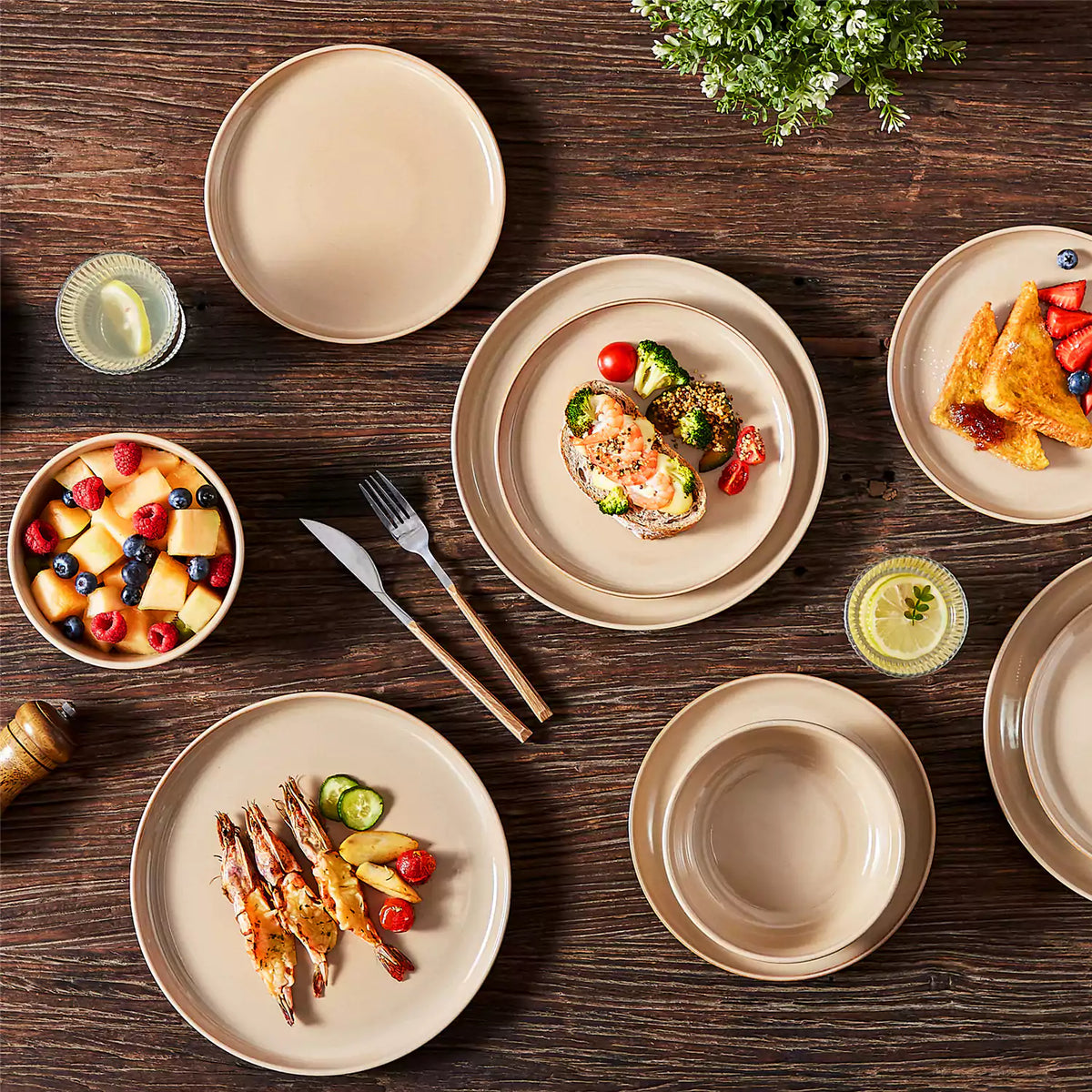 Playa 24-piece glossy reactive glaze stoneware dinnerware set with plates and bowls on dark brown table with baked shrimp, fruit bowl, and small cake.