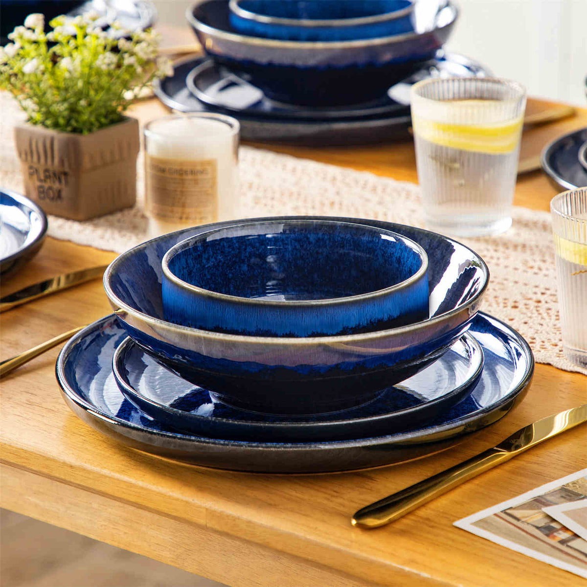 Solo dining set stacked on a wooden table, accented with a lace table runner, scented candles, and a refreshing glass of lemonade.