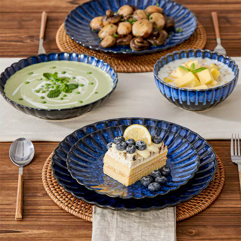 Adonis 16 piece reactive glaze dinnerware set in teal blue with pasta steak and fruit on a wooden dining table