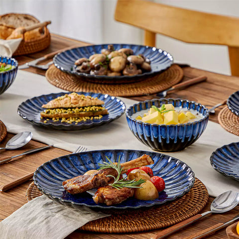 Adonis 16 piece reactive glaze dinnerware set in teal blue with pasta steak and fruit on a wooden dining table