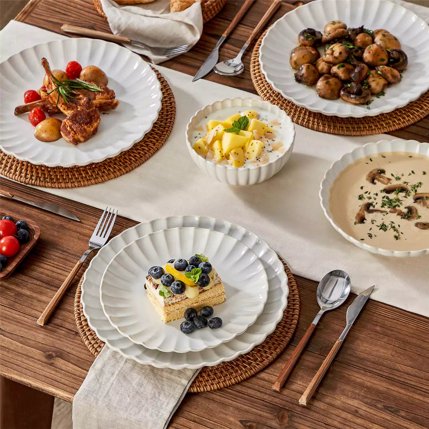Adonis 16 piece reactive glaze dinnerware set in beige with pasta steak and fruit on a wooden dining table