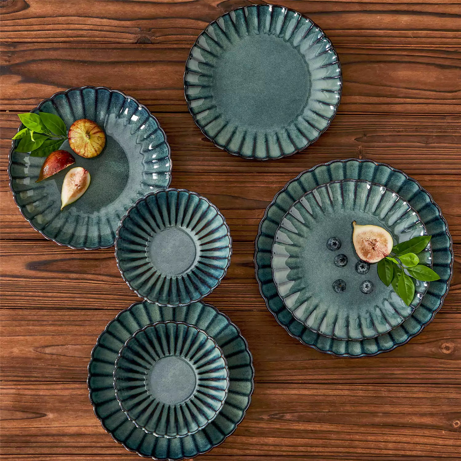 Adonis 16 piece reactive glaze dinnerware set in teal green with pasta steak and fruit on a wooden dining table