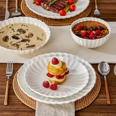 Adonis 16 piece white porcelain dinnerware set with steak pasta and fruit on a wooden dining table