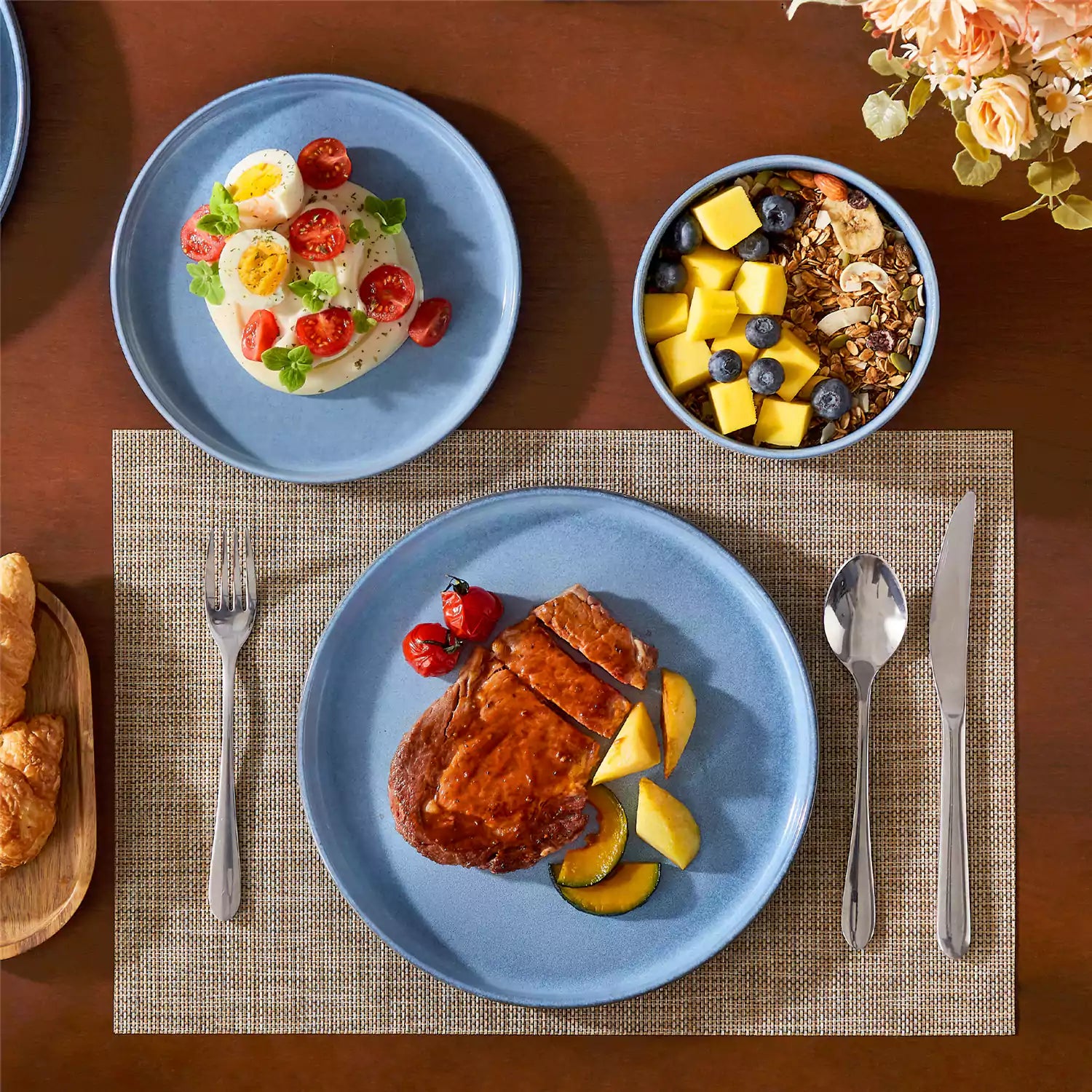 Anya 12 piece straight edge stoneware dinner set in blue with food on a rustic farmhouse wooden table with a side salad and cutlery