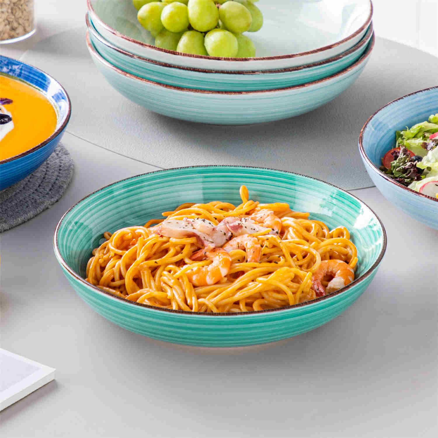 Blue Bonita large stoneware bowls set of 6 on a white table - each filled with pasta - pumpkin soup - and fruit salad - creating a bright and inviting table setting