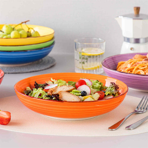Multicolor Bonita large stoneware bowls set of 6 on a white table - each filled with pasta - pumpkin soup - and fruit salad - creating a bright and inviting table setting