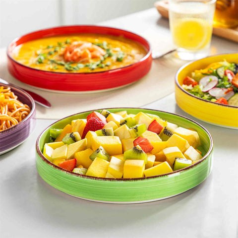 Bonita straight-edge pasta bowls set of 4 on a white table - filled with spaghetti - fruit salad - and mango - accompanied by a small honey jar - ibrant stoneware in rainbow blues