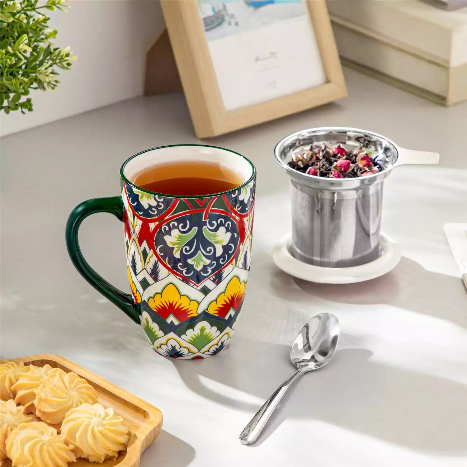 Lumi forest green porcelain tea mug with infuser and lid featuring vibrant Bohemian pattern on a wooden desk with laptop and plant