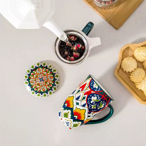 Lumi forest green porcelain tea mug with infuser and lid featuring vibrant Bohemian pattern on a wooden desk with laptop and plant