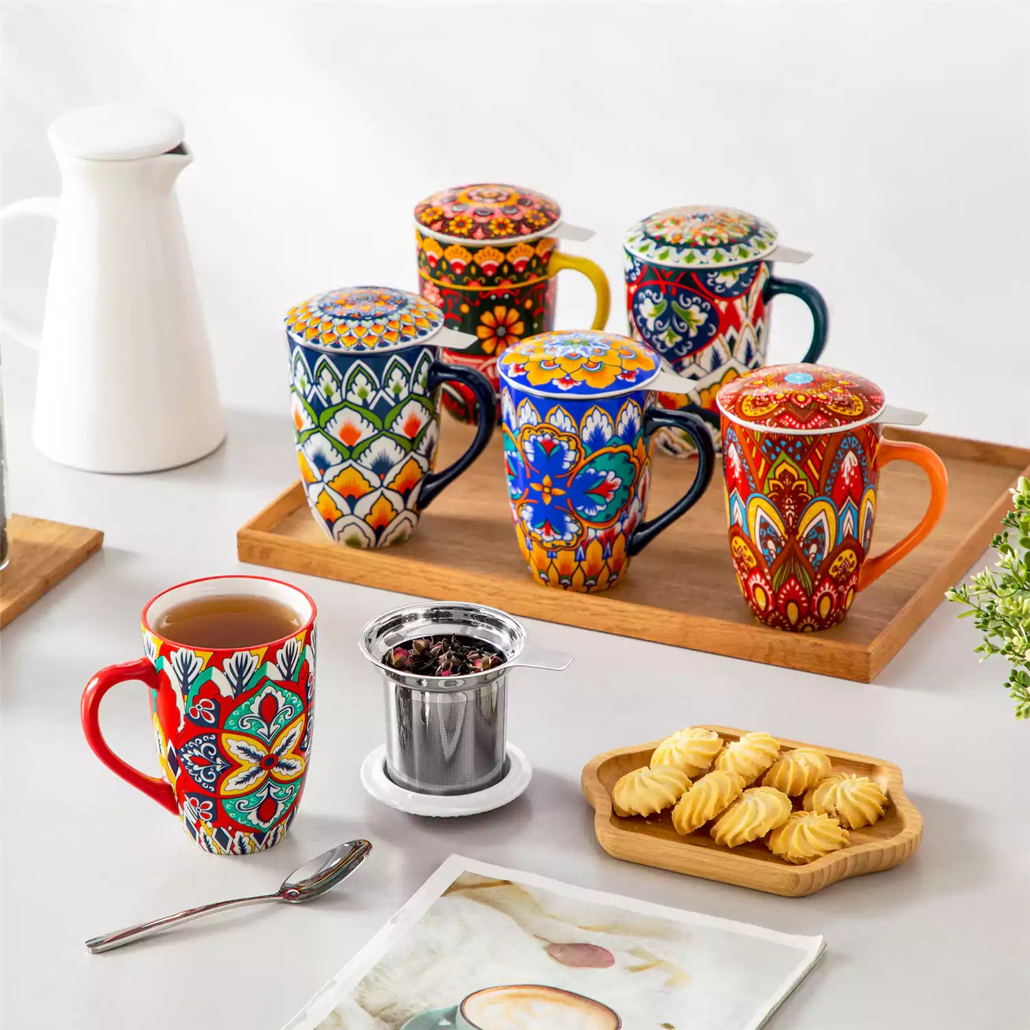 Lumi flame red porcelain tea mug with infuser and lid featuring vibrant Bohemian pattern on a wooden desk with laptop and plant