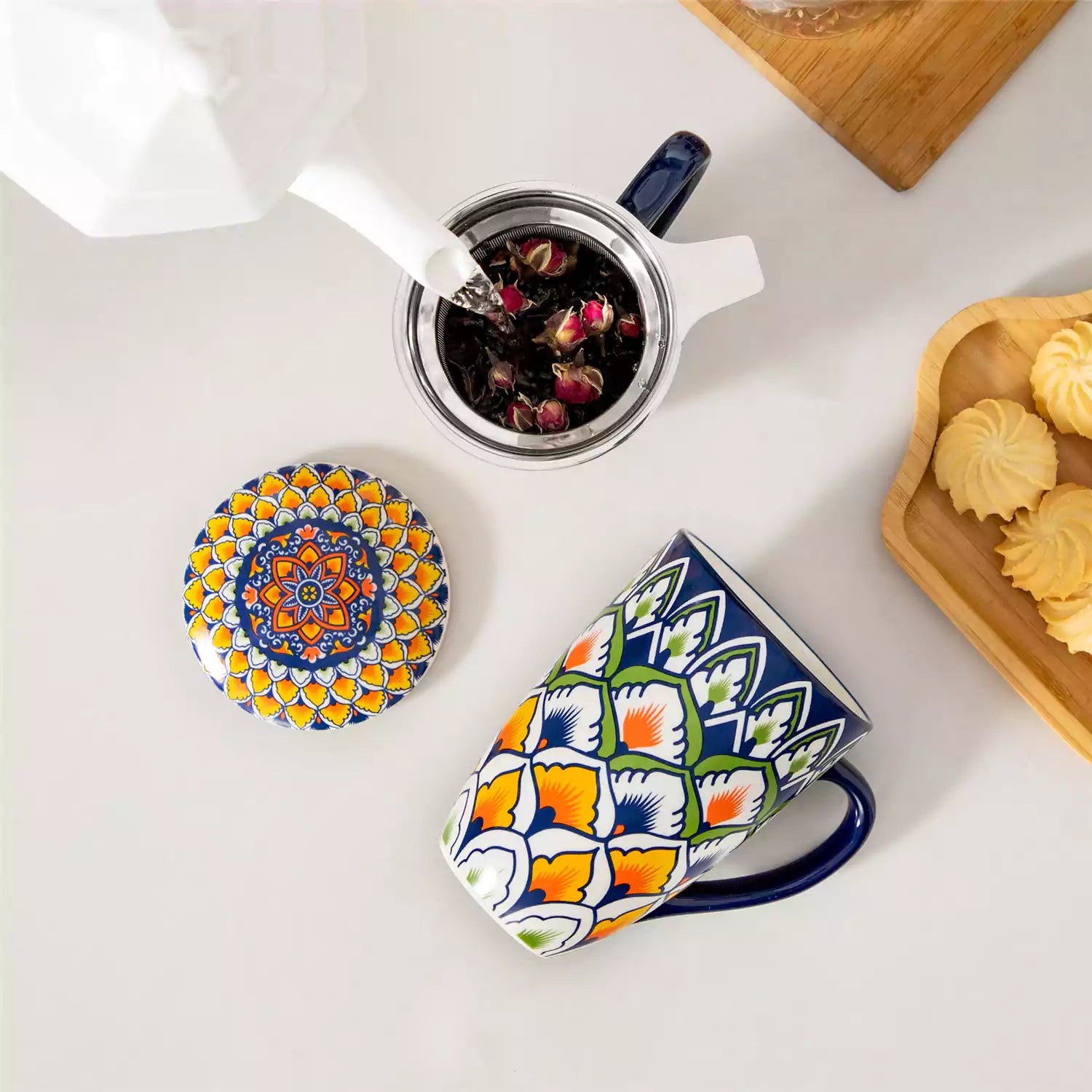 Lumi hunter green porcelain tea mug with infuser and lid featuring vibrant Bohemian pattern on a wooden desk with laptop and plant