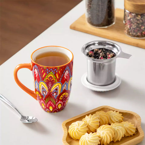 Lumi bold orange porcelain tea mug with infuser and lid featuring vibrant Bohemian pattern on a wooden desk with laptop and plant