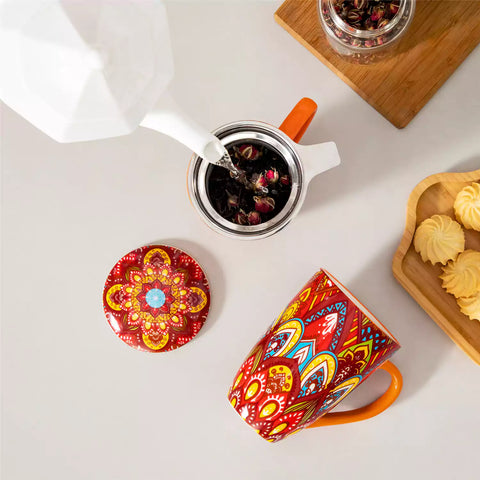 Lumi bold orange porcelain tea mug with infuser and lid featuring vibrant Bohemian pattern on a wooden desk with laptop and plant