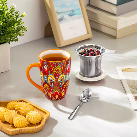 Lumi bold orange porcelain tea mug with infuser and lid featuring vibrant Bohemian pattern on a wooden desk with laptop and plant