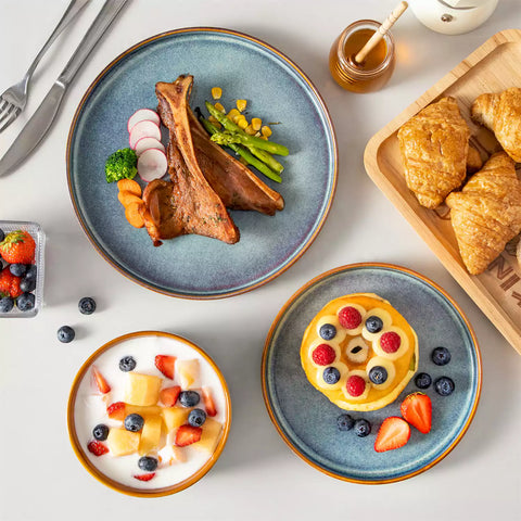 A rustic breakfast spread featuring a plate of meat with vegetables - waffles topped with fruit - and assorted pastries on a white table - complemented by blue stoneware dinnerware
