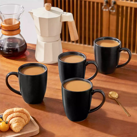 Playa set of four black stoneware mugs and a classic Moka pot on a wooden tray with a morning brew beside fresh pastries and coffee beans
