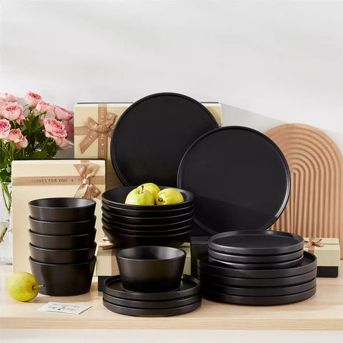 Modern black stoneware bowl and plate set displayed on a marble countertop - with a fresh salad blurred in the background - vancasso