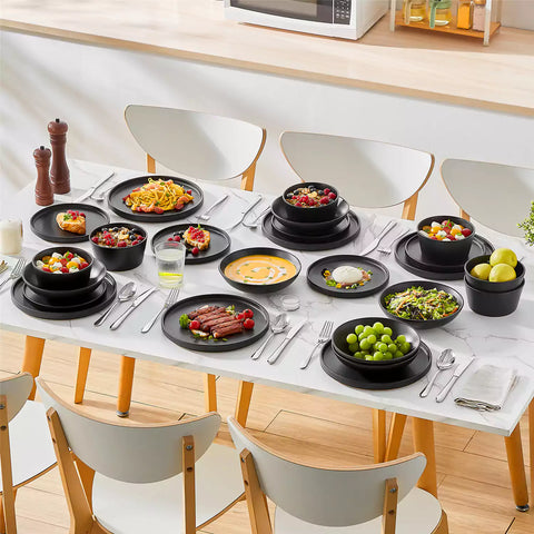 Modern black stoneware bowl and plate set displayed on a marble countertop - with a fresh salad blurred in the background - vancasso