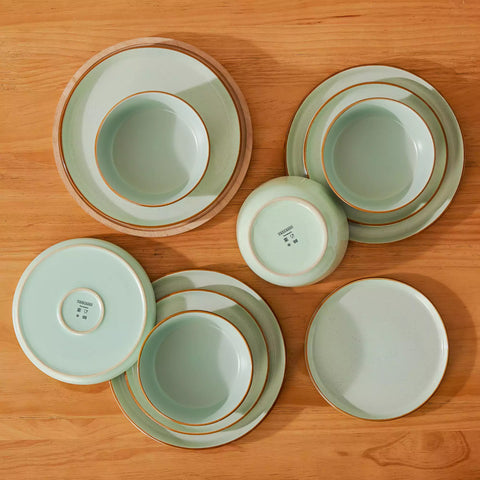 Green rustic stoneware dinnerware set with speckled - lipped-edge plates and bowls on a dining table with flowers and cutlery in a cozy modern kitchen-vancasso