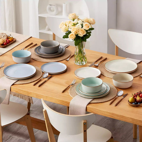 Assorted rustic stoneware dinnerware set with speckled - lipped-edge plates and bowls on a dining table with flowers and cutlery in a cozy modern kitchen-vancasso