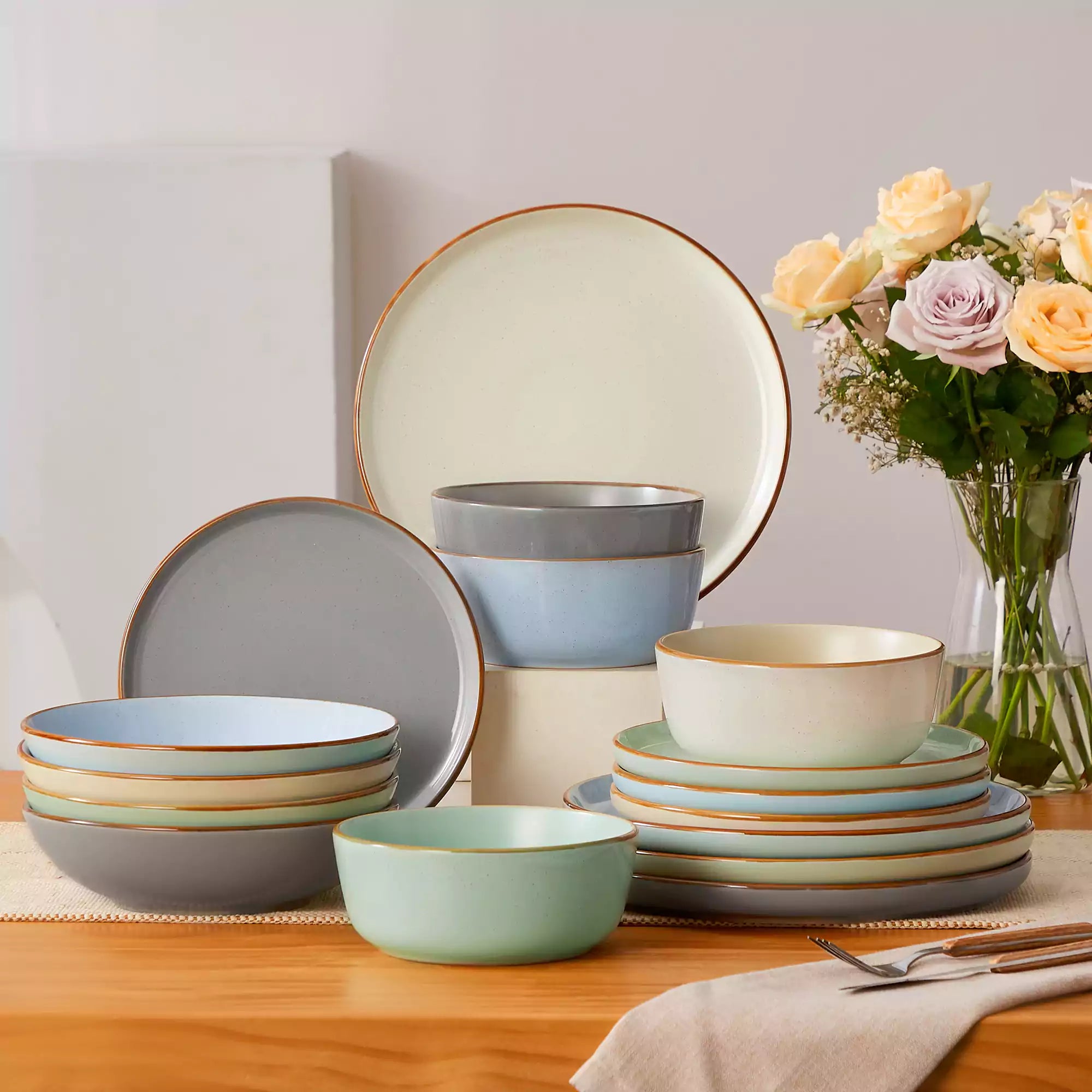 Rustic assorted speckled stoneware dinnerware set with lipped-edge plates and bowls arranged on a sunlit modern dining table-vancasso