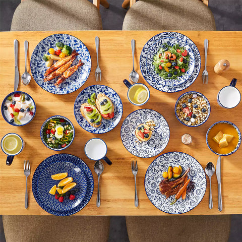 Selene 16-piece porcelain set in indigo patterns - showcasing plates - bowls - and mugs beautifully styled with vibrant meals on a rustic wooden table