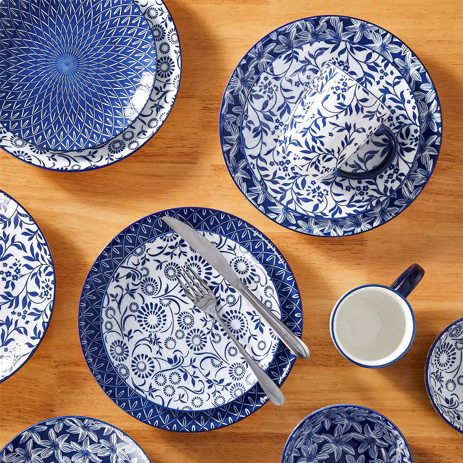 Selene 16-piece porcelain set in indigo patterns - showcasing plates - bowls - and mugs beautifully styled with vibrant meals on a rustic wooden table