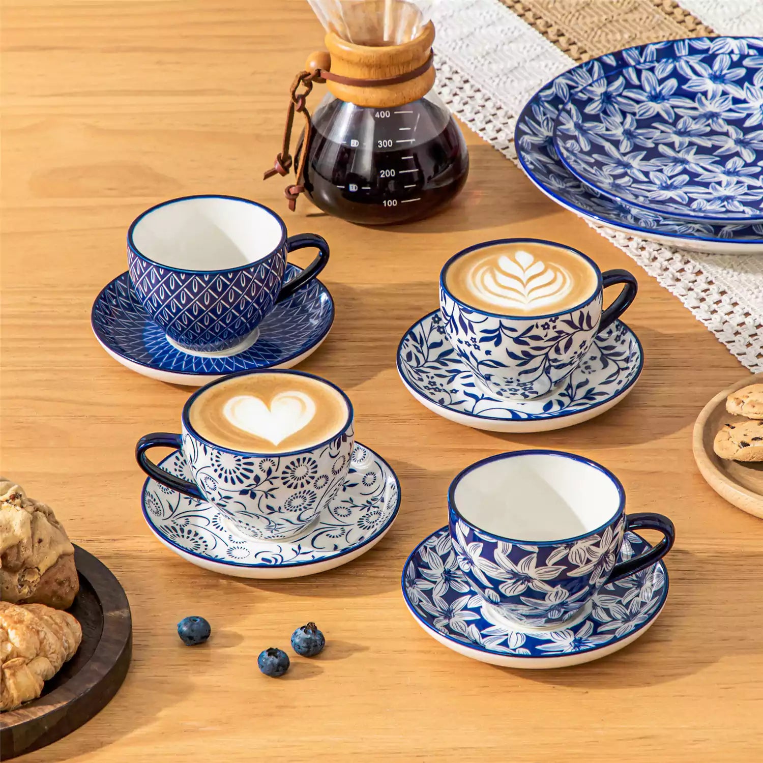 Set of 4 Selene indigo floral porcelain cups and saucers on a wooden table with coffee and pastries featuring blue and white Japanese style mix and match patterns