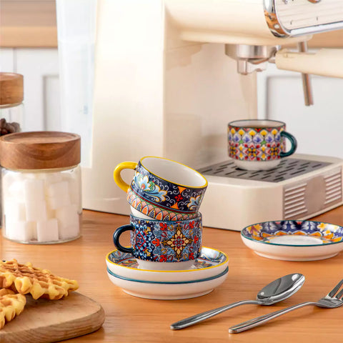 Simi 12 piece porcelain espresso set with 3oz cups and saucers in vibrant boho chic floral patterns on a black metal storage rack with a magazine and napkin on a wooden table