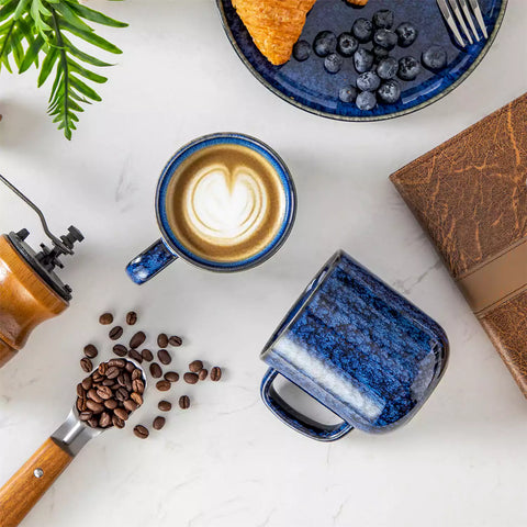Starry gently curved blue mugs set of 6 displayed on a wooden table with a coffee maker and a plate of pastries