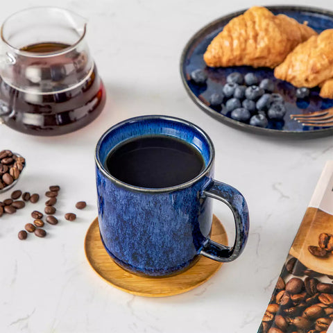 Starry gently curved blue mugs set of 6 displayed on a wooden table with a coffee maker and a plate of pastries