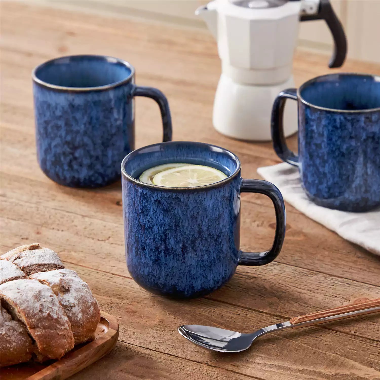 Four starry blue 16oz stoneware mugs with latte art on wooden table beside coffee brewing equipment