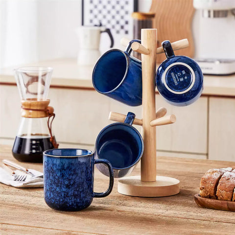 Four starry blue 16oz stoneware mugs with latte art on wooden table beside coffee brewing equipment