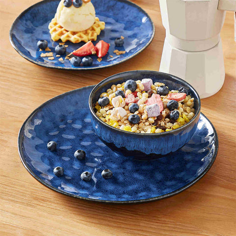 Starry 12-piece stoneware dinnerware set in blue on a light wooden table - styled with lamb chops - pastries - coffee pot - and lemon water for a cozy farmhouse breakfast scene