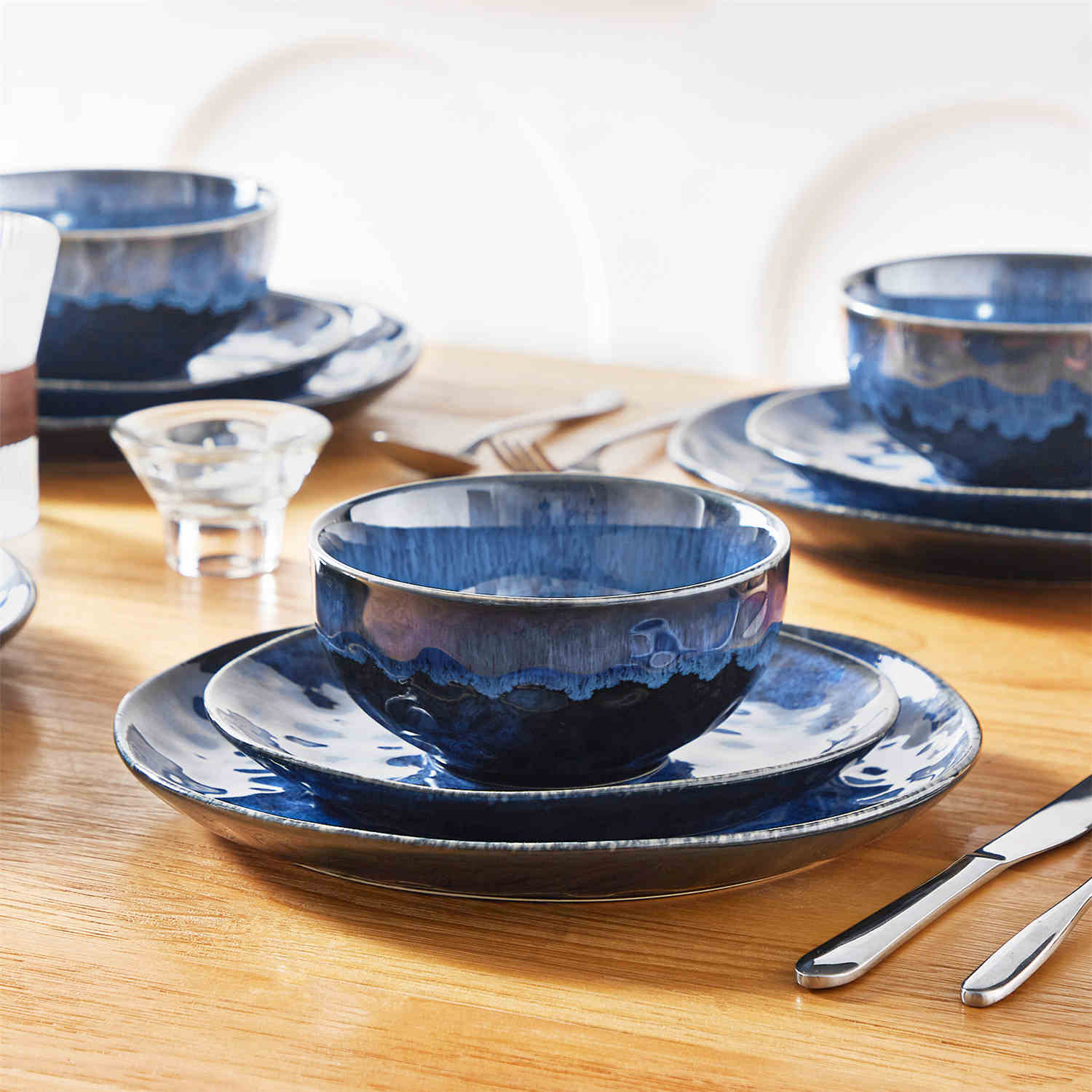 Starry 12-piece stoneware dinnerware set in blue on a light wooden table - styled with lamb chops - pastries - coffee pot - and lemon water for a cozy farmhouse breakfast scene