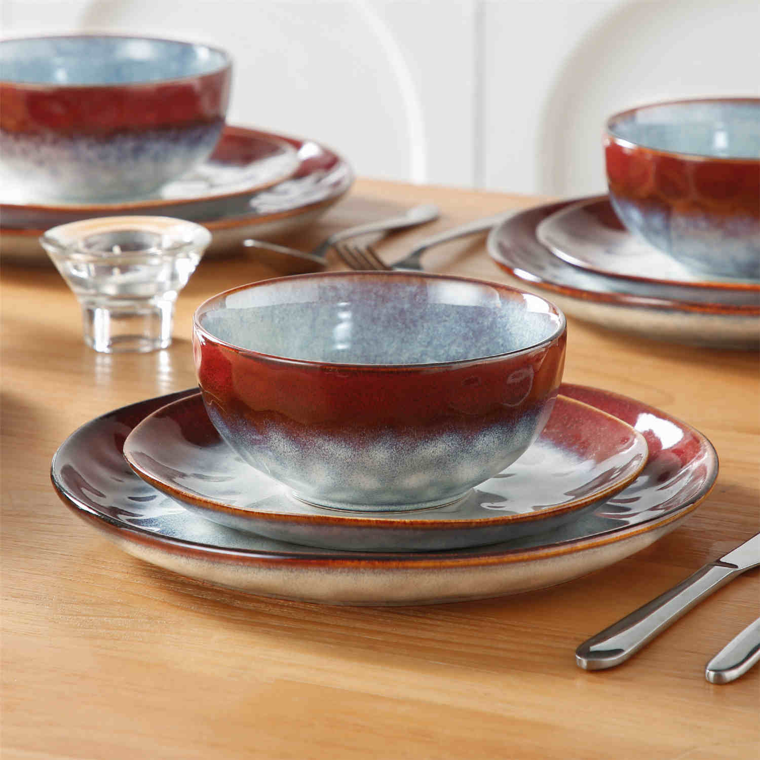 Starry 12-piece stoneware dinnerware set in red on a light wooden table - styled with lamb chops - pastries - coffee pot - and lemon water for a cozy farmhouse breakfast scene
