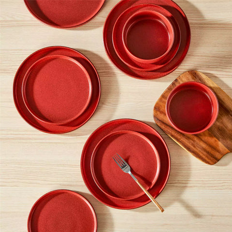 Red reactive glaze stoneware dinner plates styled with food on rustic wood table with woven placemats modern minimalist tableware set